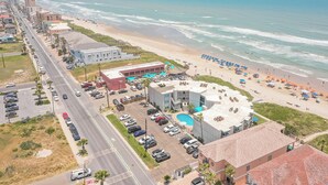 A coastal hotel with a swimming pool, beach access, and a parking lot.