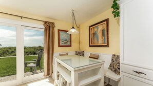 Un coin repas avec une table en verre, des chaises blanches et une vue sur l’extérieur.