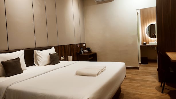 Une chambre d’hôtel avec un grand lit, une table de chevet, un bureau, une chaise, un miroir et un appareil de climatisation.