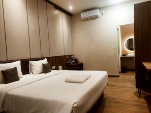 Une chambre d’hôtel avec un grand lit, une table de chevet, un bureau, une chaise, un miroir et un appareil de climatisation.