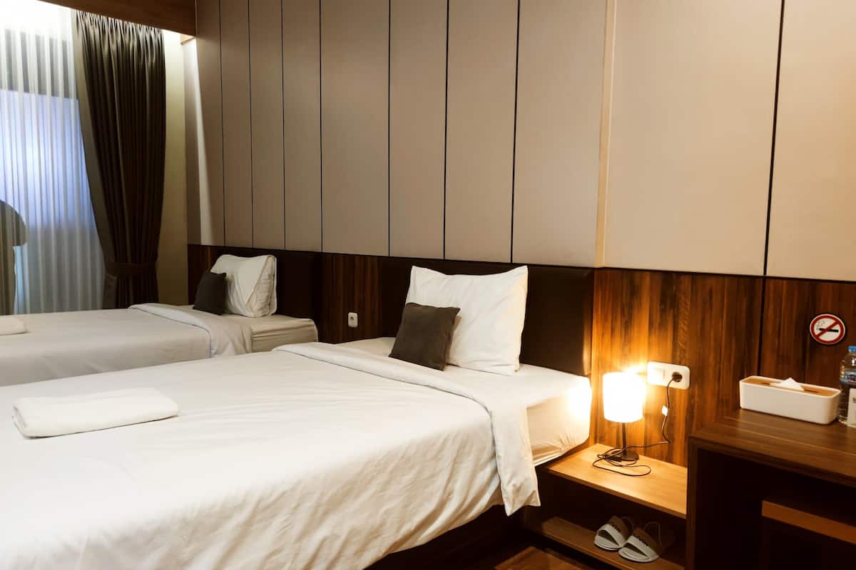 Een hotelkamer met twee bedden, een nachtkastje met een lamp, een houten hoofdeinde en een schoenenrek.