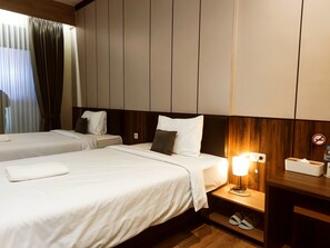Une chambre d’hôtel avec deux lits, une table de chevet avec une lampe, une tête de lit en bois et un porte-chaussures.