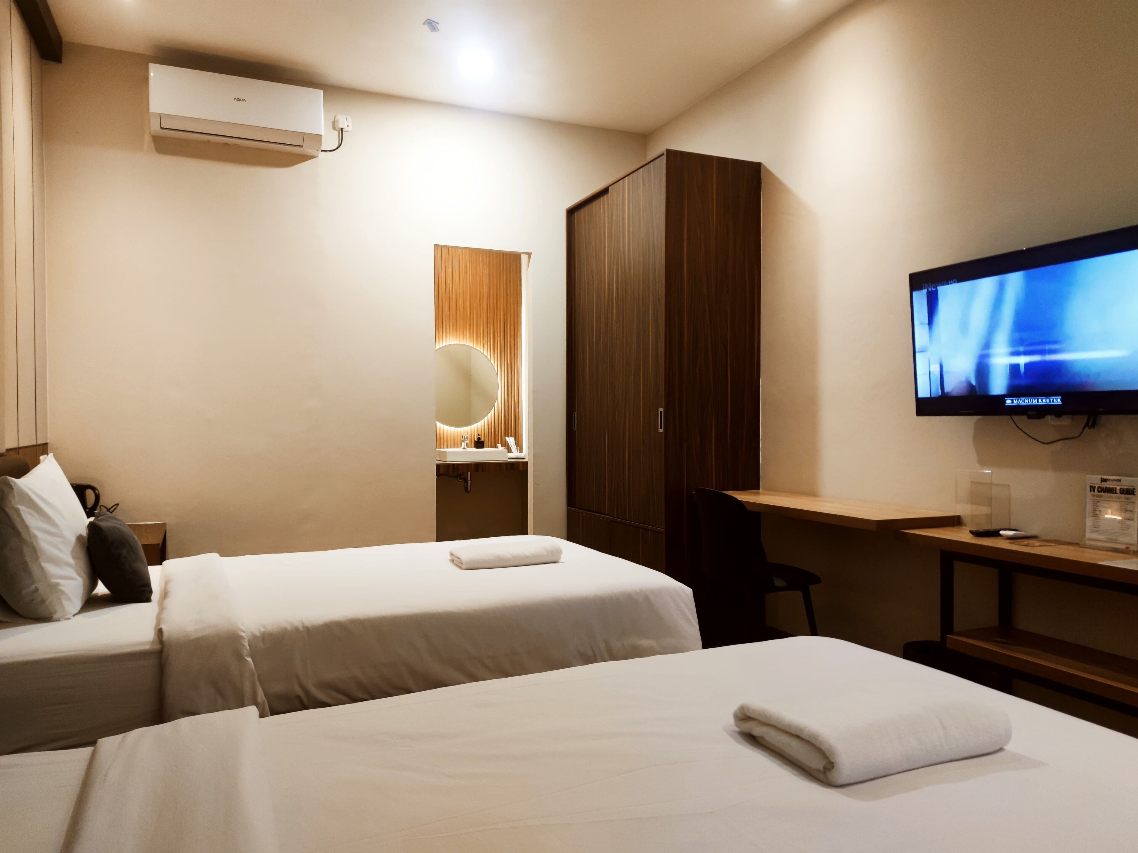 A hotel room with two beds, a desk, a TV, a wardrobe, and a bathroom with a mirror.