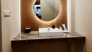 Une salle de bain avec un miroir rond, un lavabo blanc et un mur recouvert de panneaux en bois.