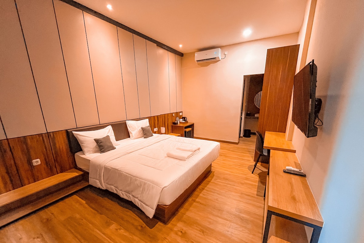 Een moderne hotelkamer met een groot bed, houten vloeren, een bureau en een televisie.