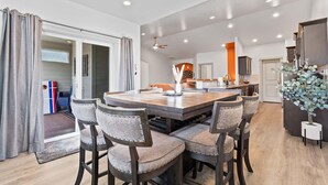 A modern dining area with a large table and six upholstered chairs, a ceiling fan, and a kitchen in the background. - A Motown-Inspired Vinyl Retreat (Meridian)