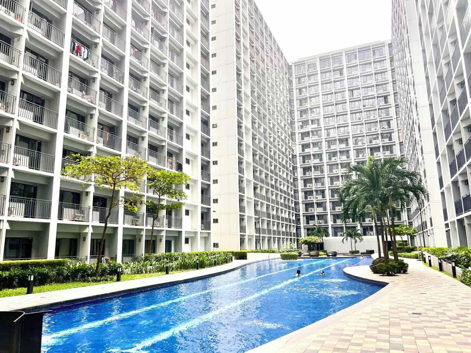 A modern apartment building with a swimming pool, surrounded by greenery and palm trees.