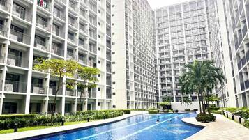 A modern apartment building with a swimming pool, surrounded by greenery and palm trees.