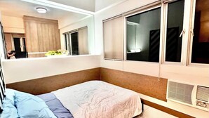 Un dormitorio con una cama, un ventanal grande, un espejo y un radiador.