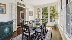 A dining room with a round table, chairs, and a large window with a view of trees and parked cars. - Charming Historic Estate | In-town location (Portland)