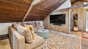 An attic room with a wooden ceiling, a large TV mounted on the wall, a sofa, and a patterned rug. - Charming Historic Estate | In-town location (Portland)