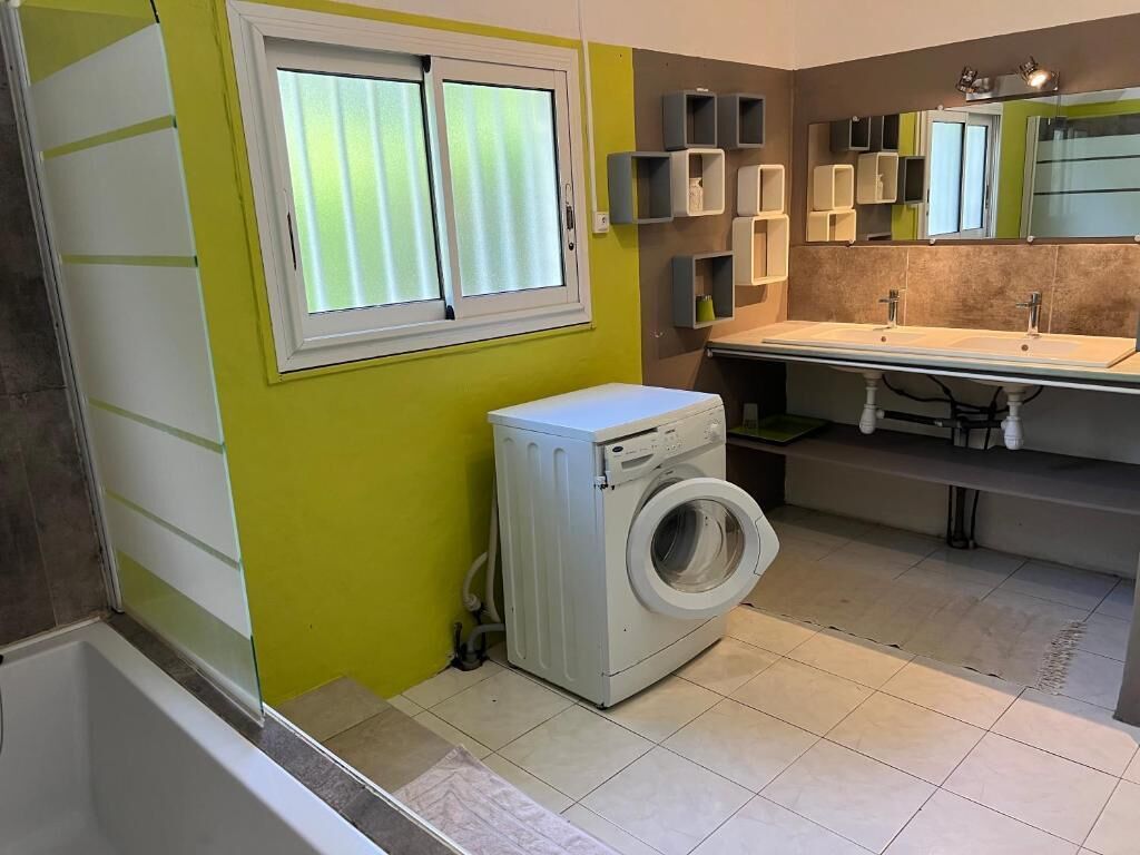 Une petite salle de bain équipée d’un lave-linge, d’un lavabo et d’une fenêtre avec des stores.