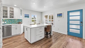 Cocina moderna con armarios blancos, una isla grande y una puerta azul.