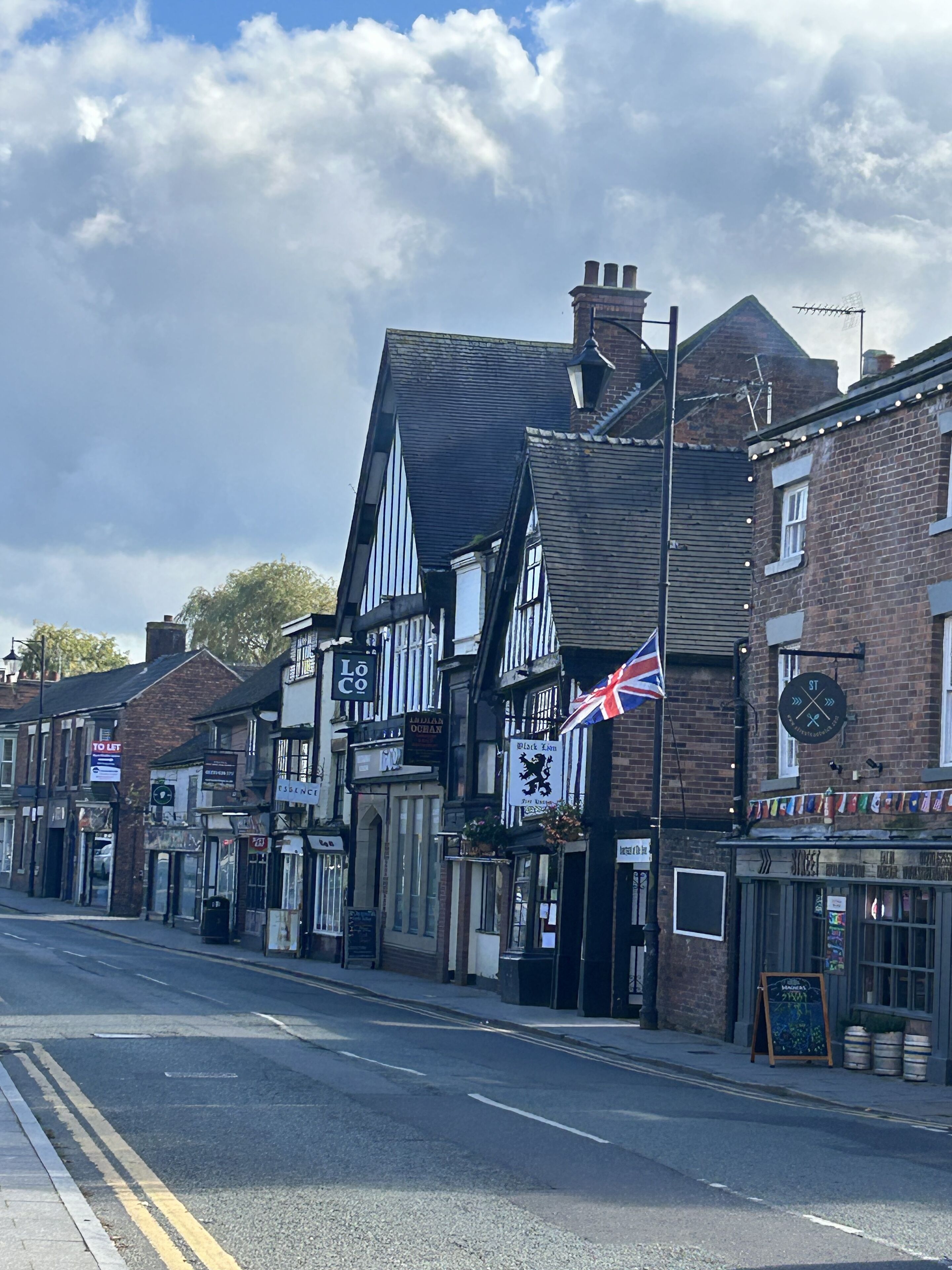 Une rue bordée de bâtiments traditionnels, dont un pub orné d’un drapeau britannique et d’une enseigne représentant un « Lion noir ».