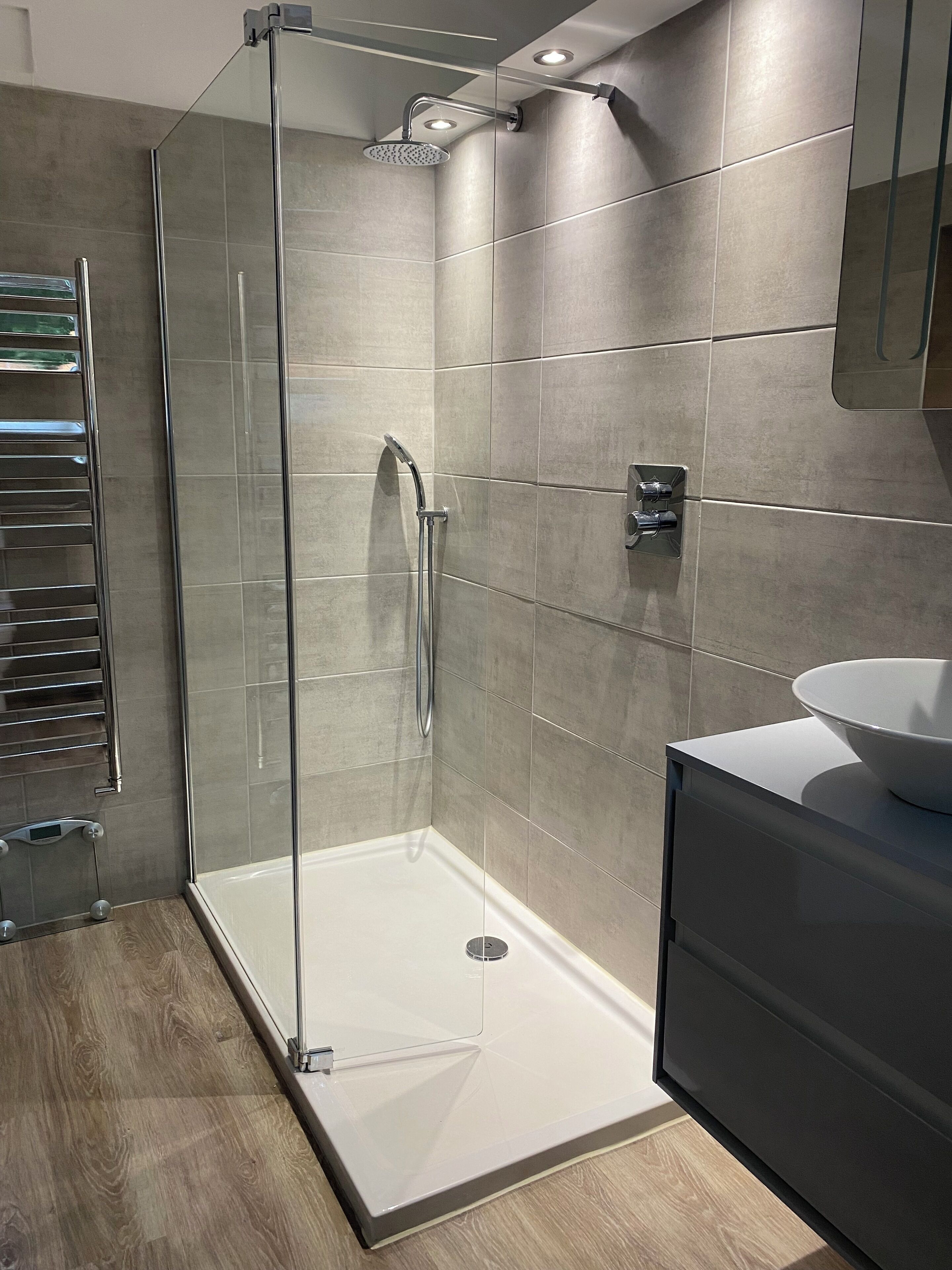 A modern bathroom with a glass-enclosed shower, a white sink, and a wooden floor.