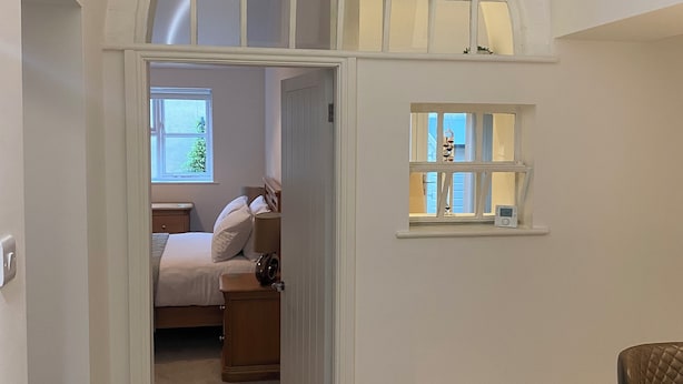 A narrow hallway with a wooden floor leading to a bedroom with a bed, bedside table, and a window. There is a small table with a chair in the foreground. - Fabulous unique accommodation within walking distance of Nantwich town centre (Nantwich)