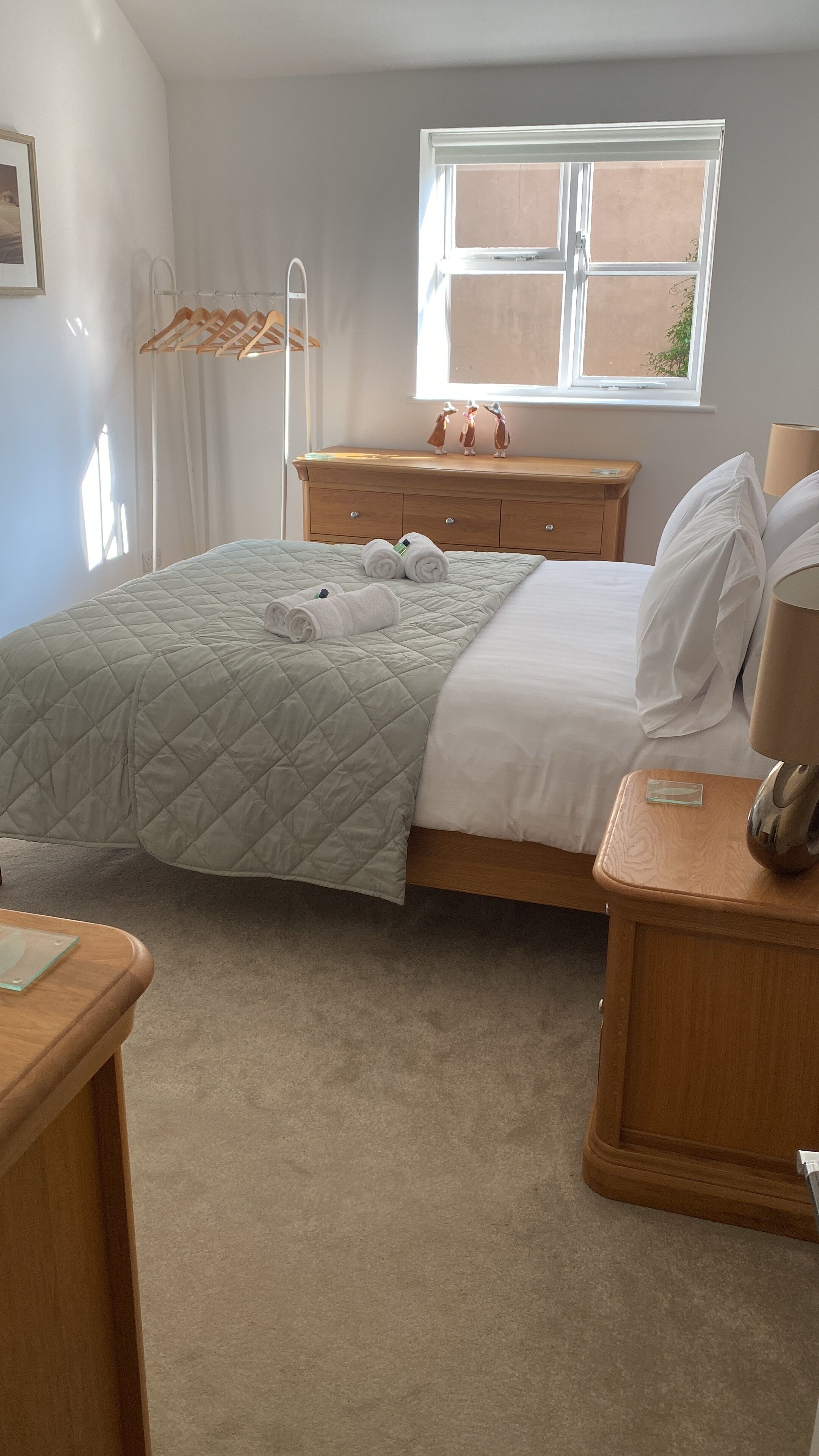 A neatly arranged bedroom with a bed, bedside tables, a dresser, and a window with a view.