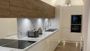 A modern kitchen with wooden cabinets, a marble countertop, a built-in oven, and a sleek black stove. - Fabulous unique accommodation within walking distance of Nantwich town centre (Nantwich)