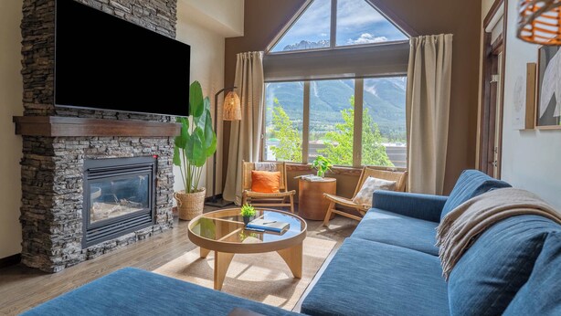 A living room with a stone fireplace, a television, a large window with a mountain view, a blue sofa, and a coffee table.