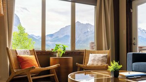 A room with a large window, wicker chairs, a small side table with a plant, and a glass-top coffee table.