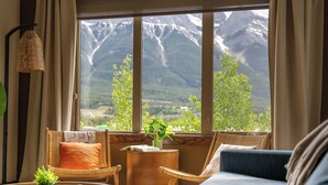 A room with a large window, wicker furniture, a small side table, and a view of mountains.
