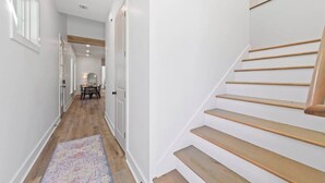 Un couloir doté d’un plancher en bois, d’un tapis à motifs et d’un escalier avec des marches en bois et une main courante.