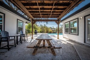 Eine überdachte Terrasse mit Picknicktisch, Stühlen und einem Grill.