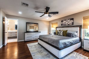 Une chambre à coucher comprenant un lit, un ventilateur de plafond, une table de chevet, une lampe, une commode et une fenêtre.