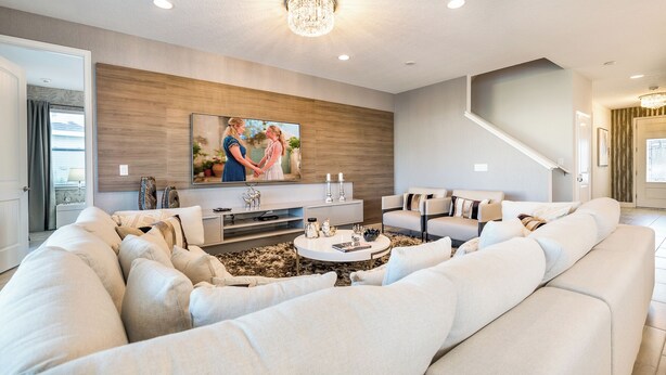 Un salon moderne avec un canapé d’angle, un téléviseur à écran plat fixé à un mur en bois, une table basse agrémentée d’objets décoratifs et un escalier menant à un autre niveau.