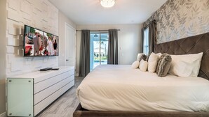 Une chambre moderne avec un grand lit, un téléviseur fixé au mur blanc et une vue sur l’extérieur grâce à une porte coulissante.