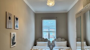 A bedroom with two beds, a ceiling light, and a window with blinds. - London City Apartment - Modern & Cozy Stay (London)