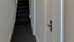 A hallway with a black carpet, white walls, and a door at the end. - London City Apartment - Modern & Cozy Stay (London)