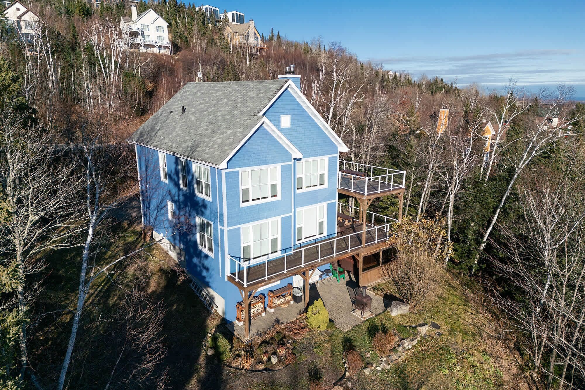 A two-story house with a balcony, surrounded by trees and a view of the water.
