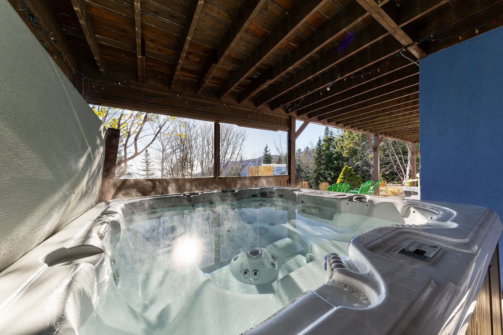 Un jacuzzi bajo una pérgola de madera, con vista a árboles y un edificio al fondo.