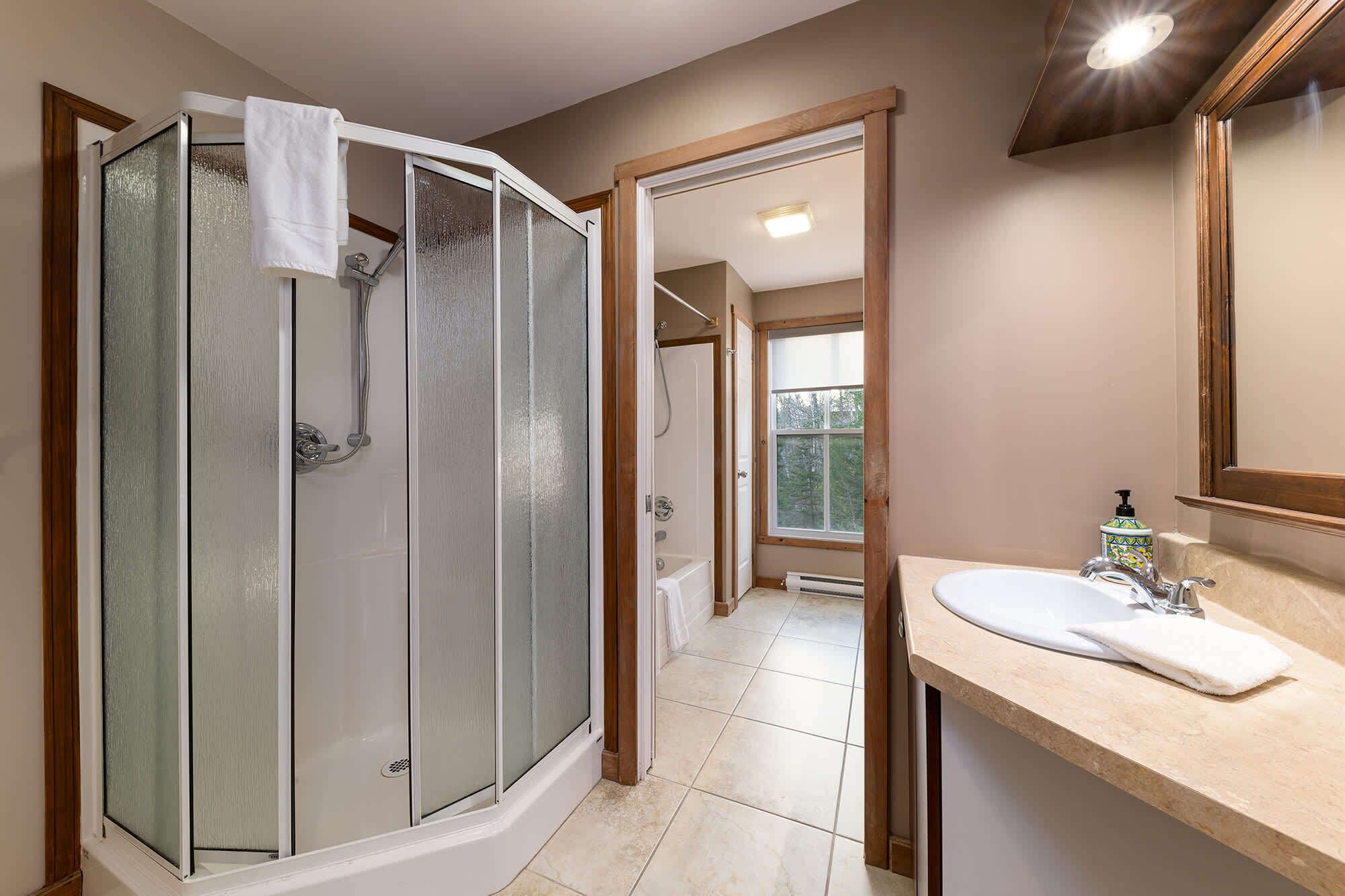 Une salle de bain dotée d’une douche à parois de verre, d’une baignoire, d’un lavabo avec un miroir et d’une fenêtre donnant sur l’extérieur.