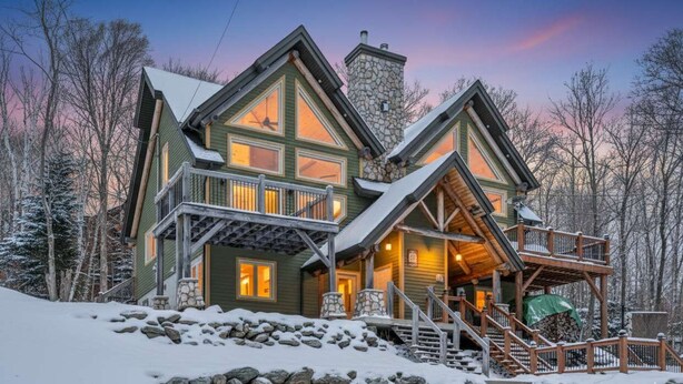 Un gran albergue de varios pisos con chimenea de piedra, balcones de madera y un paisaje cubierto de nieve.