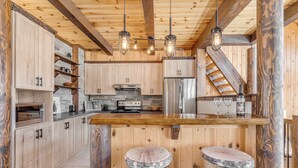 Cocina rústica con gabinetes de madera, una isla central con taburetes, horno empotrado y salpicadero de piedra.