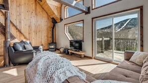 Una sala de estar acogedora con chimenea, sofá de cuero y un amplio ventanal con vistas a la montaña.
