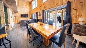 Una stanza con rivestimento in legno, un grande tavolo da pranzo, sedie, una TV e vista panoramica attraverso una porta in vetro.