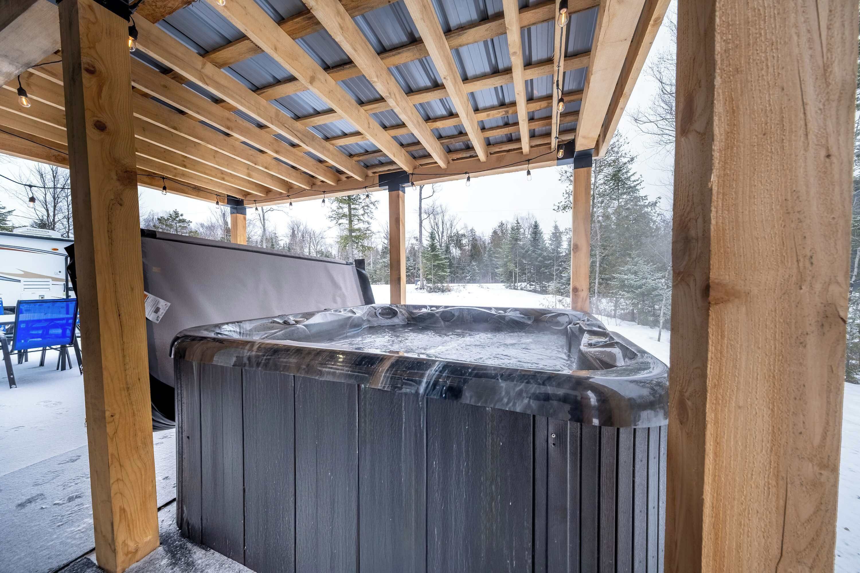 A hot tub under a wooden pergola with a snowy landscape in the background.