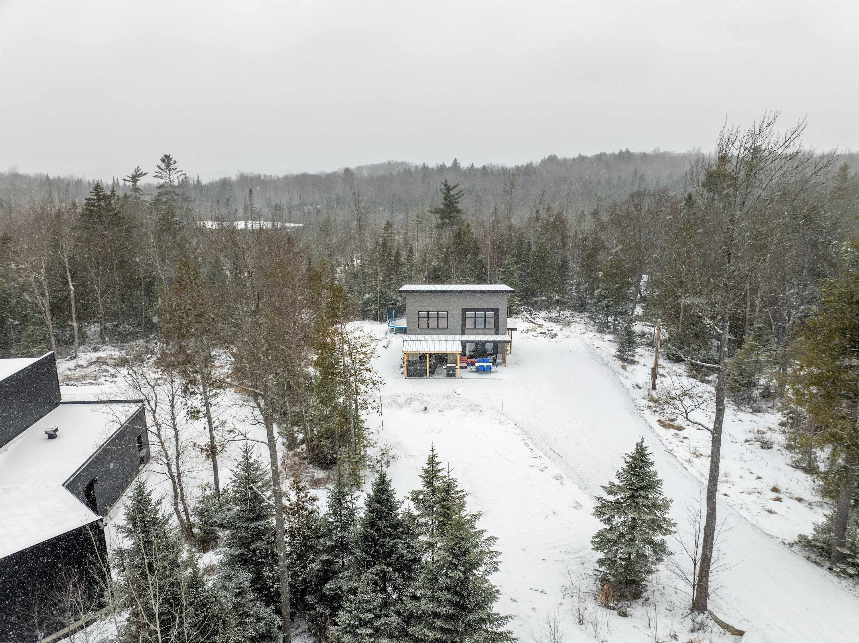 Una casa moderna con un porche cubierto, rodeada por un bosque nevado.
