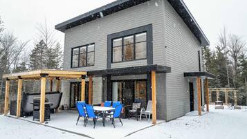 Una casa a due piani con un patio coperto, un barbecue e mobili da esterno.