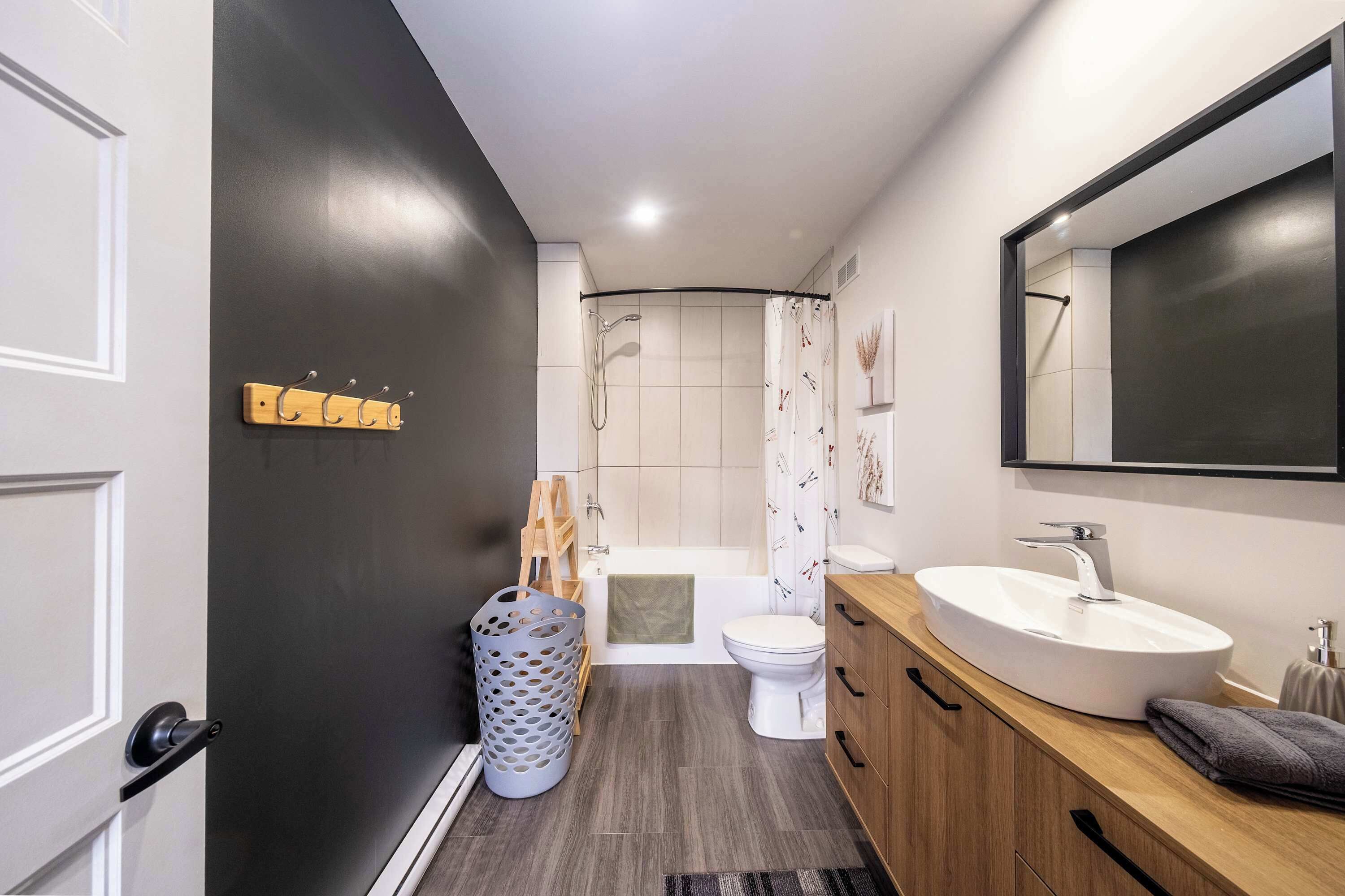 Une salle de bain moderne avec un mur de couleur sombre, un meuble-lavabo en bois, un lavabo blanc, des toilettes et un espace douche.