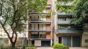 Un immeuble résidentiel à plusieurs étages, doté de balcons, d’un garage et d’un arbre au premier plan.