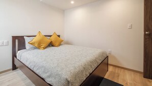 Une chambre à coucher avec un lit, deux oreillers, une tête de lit en bois, une porte en bois et un interrupteur sur le mur.