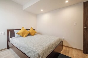 Ein Schlafzimmer mit einem Bett, zwei Kissen, einem Holzkopfstück und einer Holztür. Ein Lichtschalter befindet sich an der Wand.