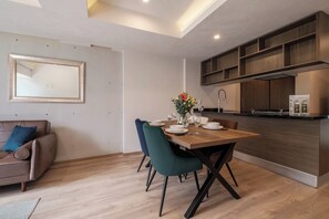 A modern kitchen with wooden cabinets, a dining area with a wooden table and chairs, and a sofa with a cushion.