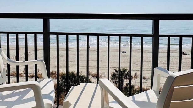 Un balcón con sillas de plástico blanco con vista a la playa.