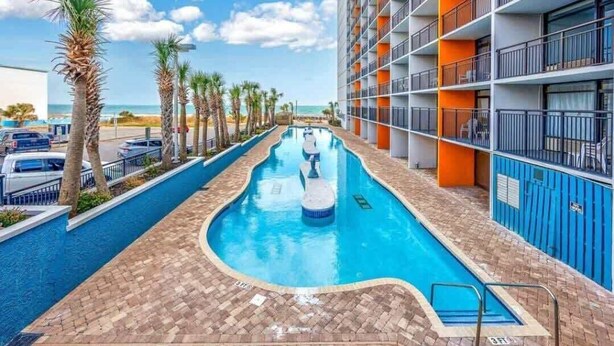 A swimming pool with a clear view of the ocean, surrounded by palm trees and a multi-story building with balconies. - LA74 Great studio right on the beach + pool (Myrtle Beach)
