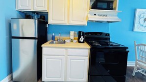 A compact kitchen with white cabinets, a stainless steel refrigerator, a black stove, and a microwave. - SM50 Bright Studio walk to the beach (Myrtle Beach)
